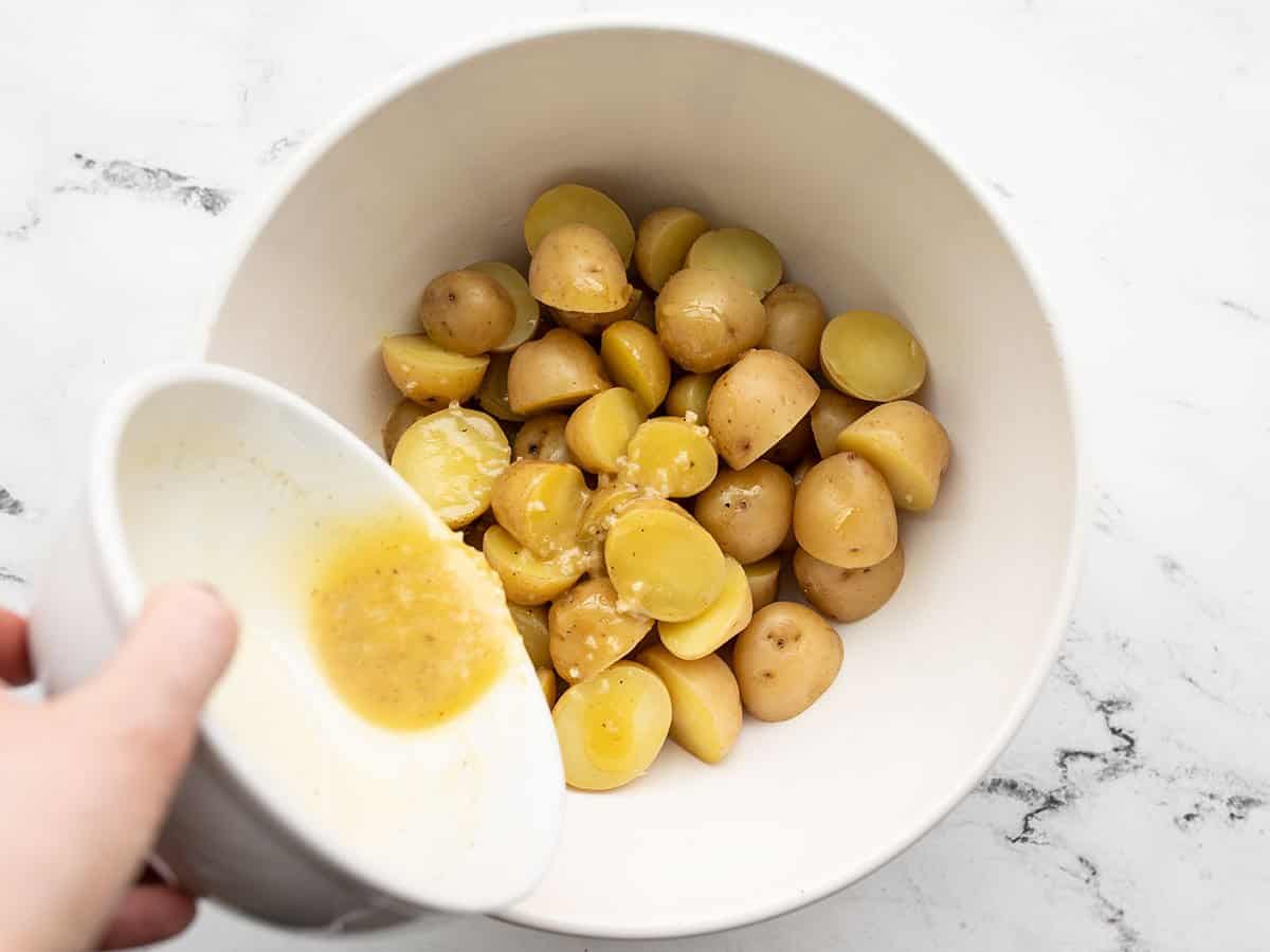 Dressing being poured over the potatoes in a bowl.