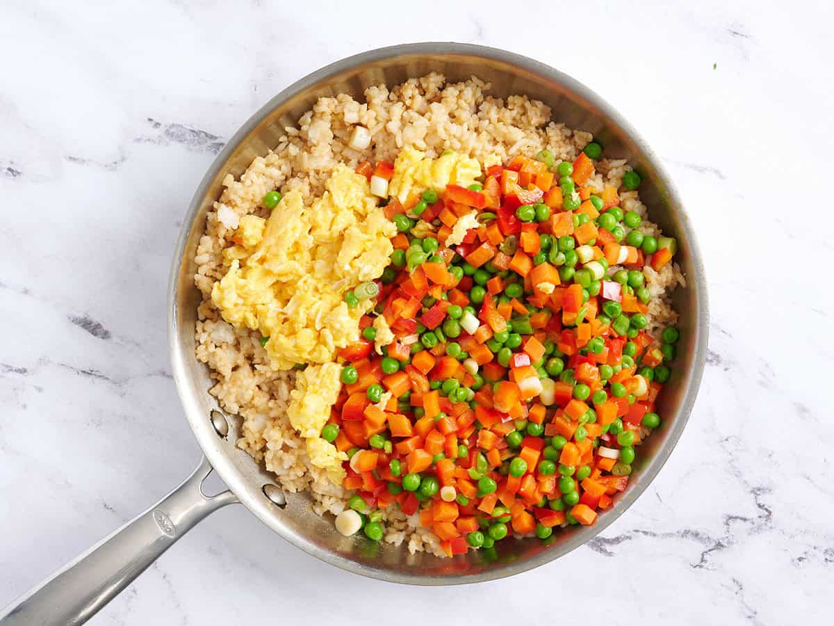 Scrambled eggs and veggies added to fried rice in a skillet.