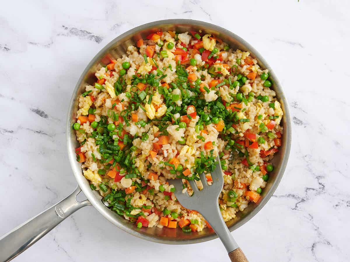 Green onions being stirred into vegetable friend rice in a skillet.