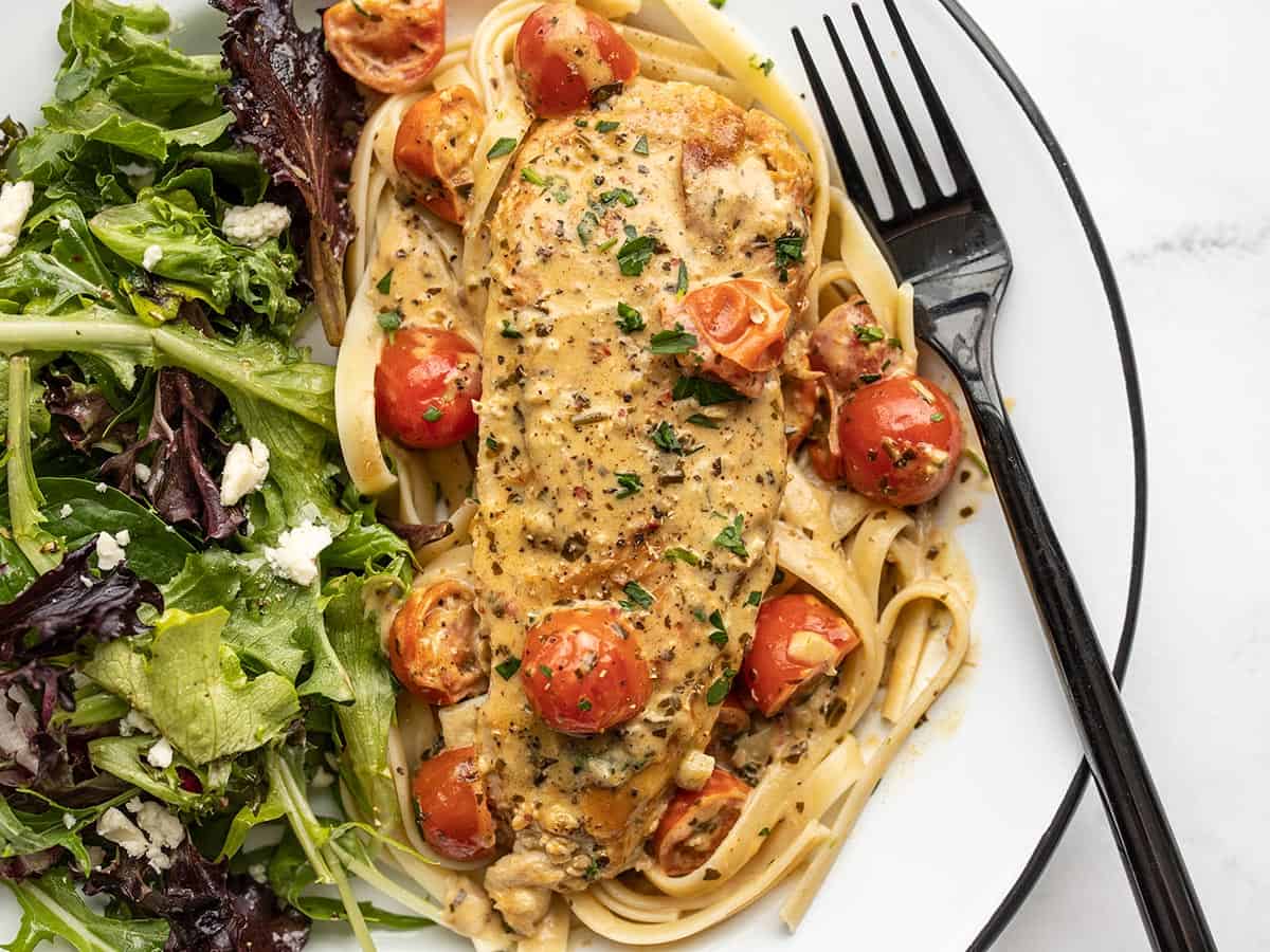 Overhead view of creamy pesto chicken on a plate with a salad.
