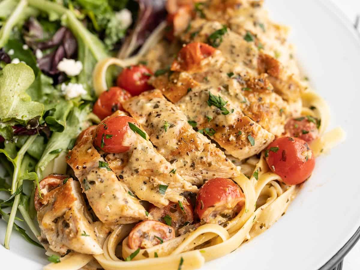 side view of sliced creamy pesto chicken on a plate with a salad.