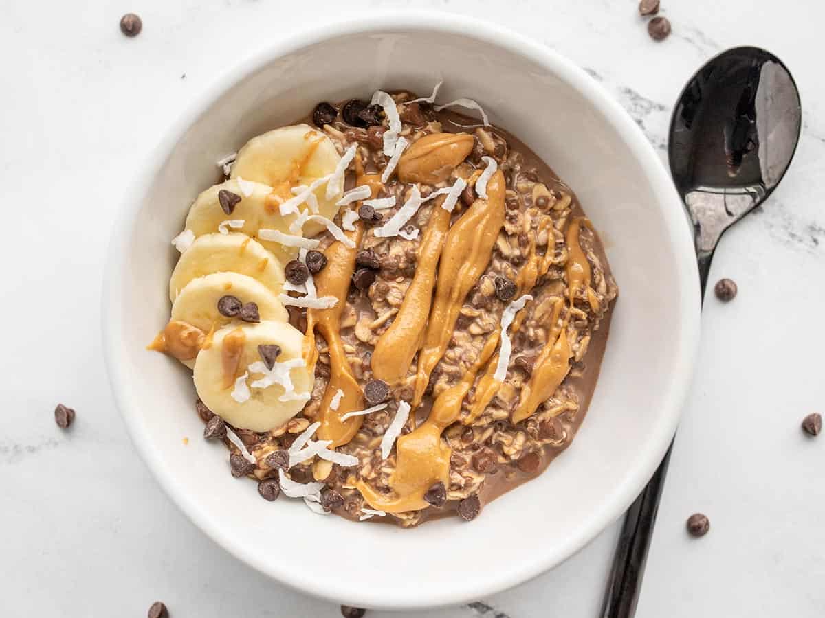 A bowl of chocolate overnight oats topped with bananas, peanut butter, and coconut.