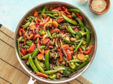 Vegetable stir fry in the skillet against a blue background.