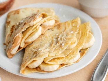 close up side view of two crepes on a plate stuffed with peanut butter and bananas.