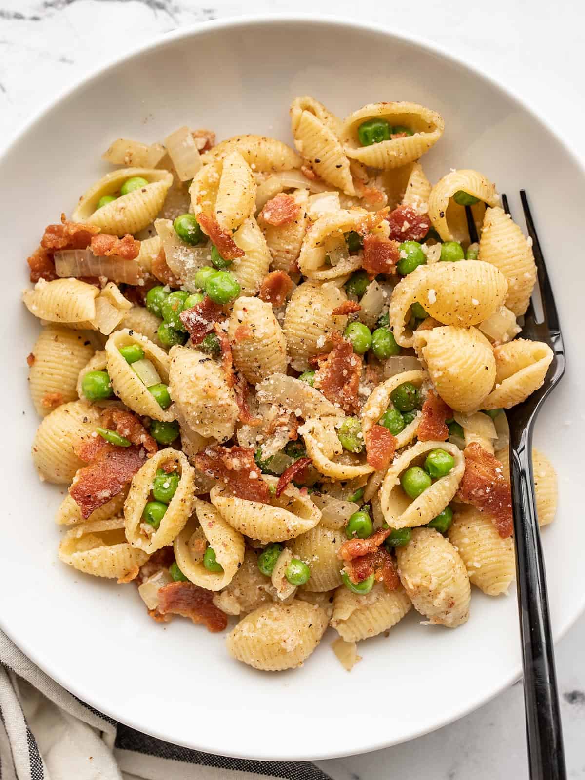 Overhead view of a bowl of pasta with bacon and peas