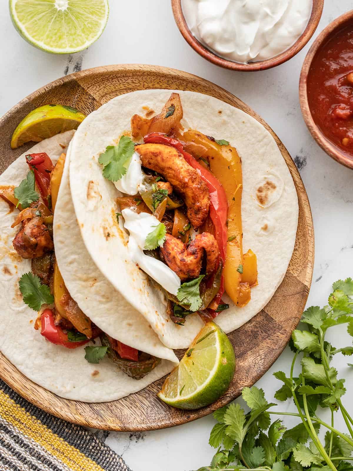 Two fajitas on a wooden plate with toppings on the sides