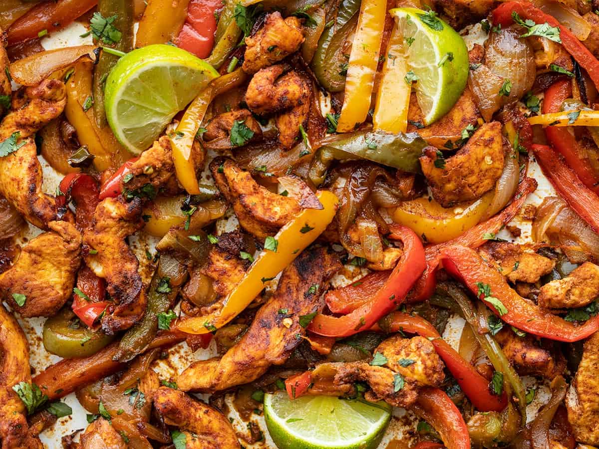 Close up of baked chicken fajita meat and vegetables with wedges of lime.
