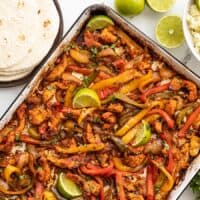 Sheet pan full of chicken fajitas with rice and tortillas on the side