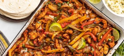 Sheet pan full of chicken fajitas with rice and tortillas on the side