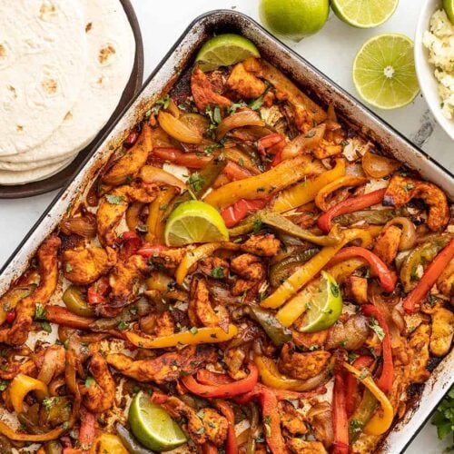Sheet pan full of chicken fajitas with rice and tortillas on the side