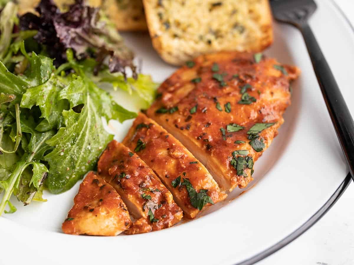 Side view of sliced chicken on a plate with garlic bread and salad.