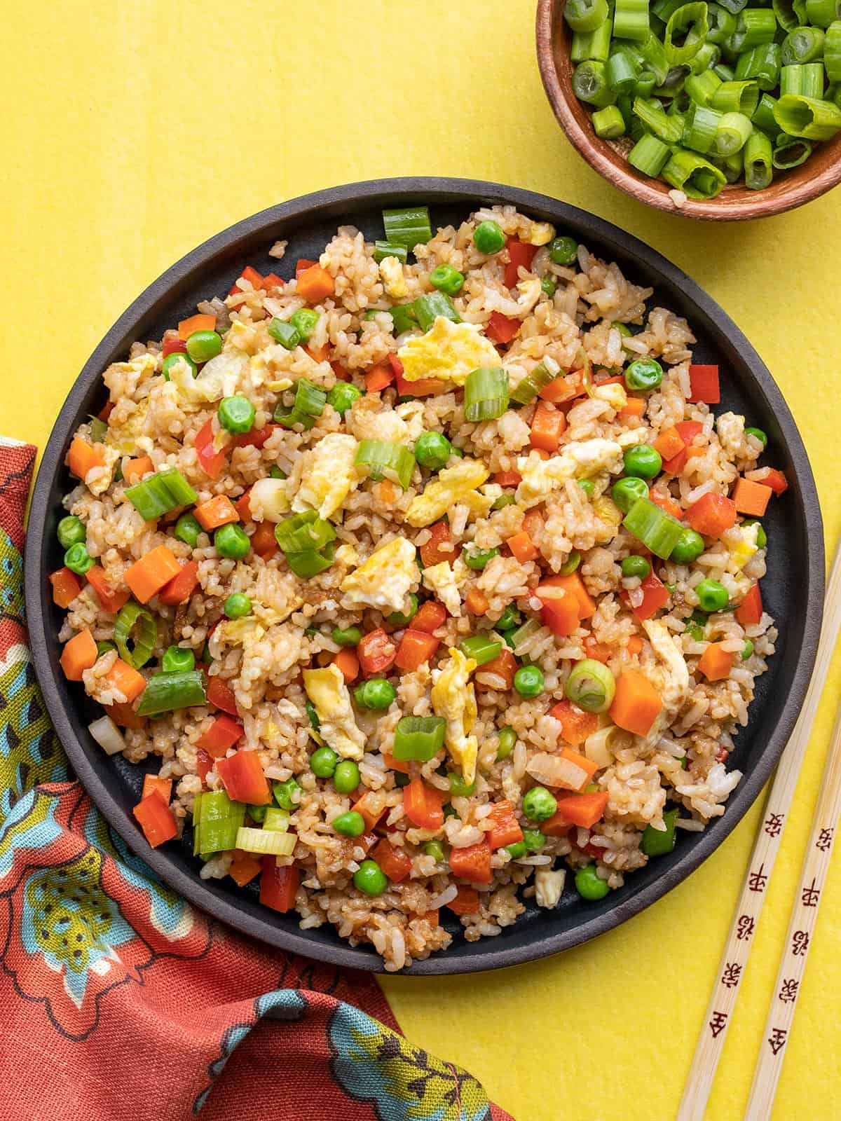 Overhead view of a black plate full of vegetable fried rice on a yellow background