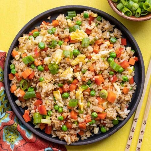 Overhead view of a plate full of vegetable fried rice on a yellow background.