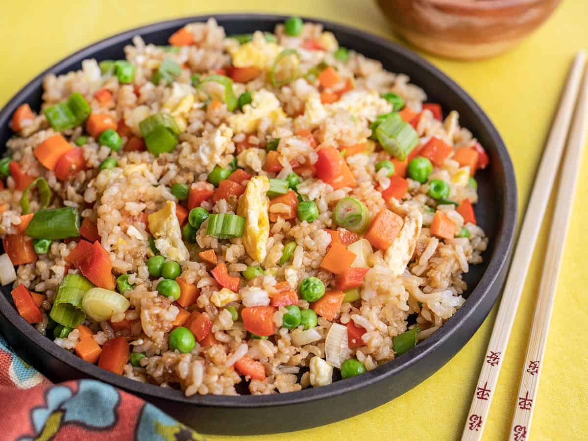 side view of a plate full of fried rice with chop sticks on the side.