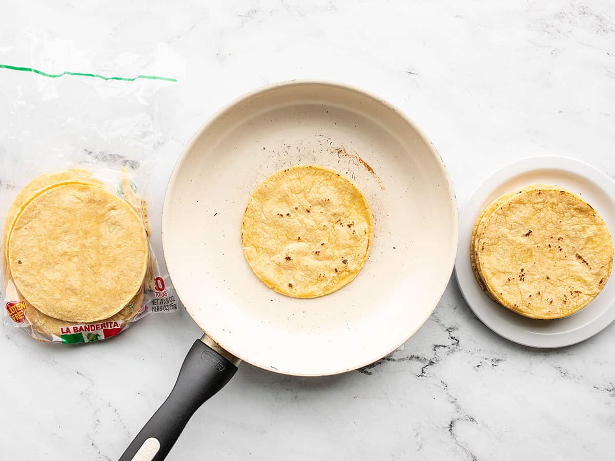 Corn tortillas being toasted in a skillet.