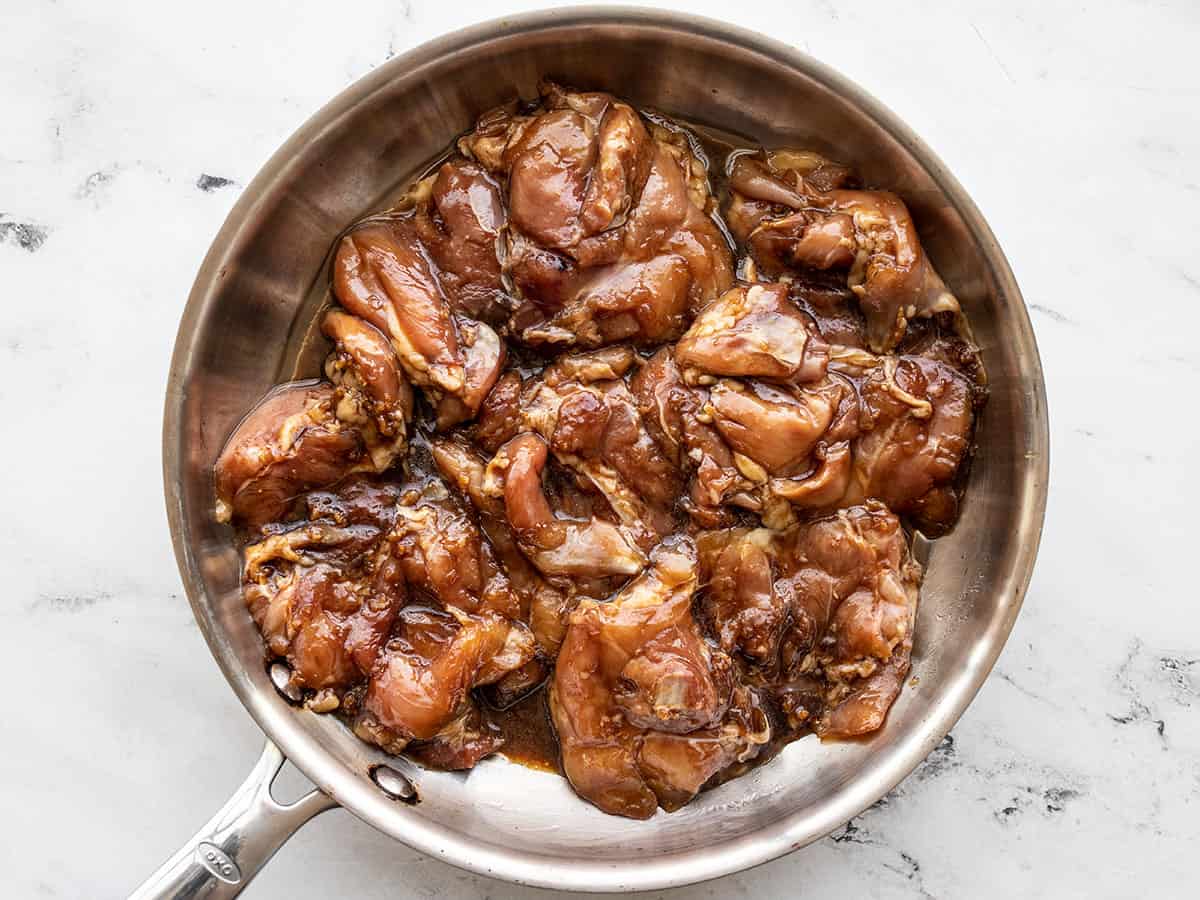 Raw marinated chicken thighs in a frying pan.