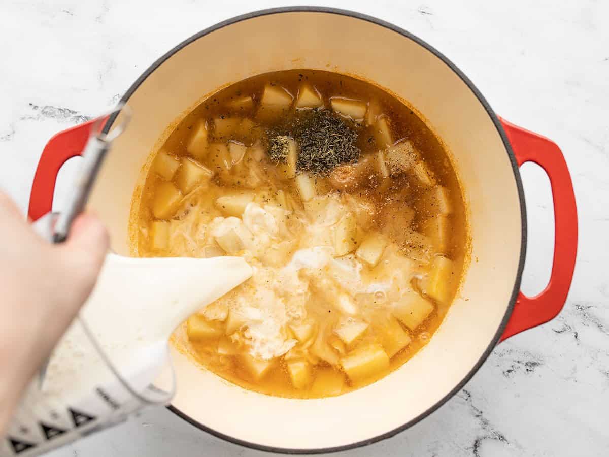 Milk being poured into the pot with potatoes and herbs.