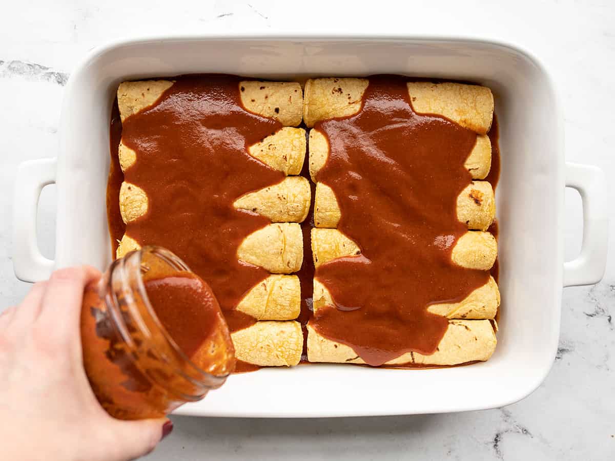 Enchilada sauce being poured over enchiladas in the casserole dish.