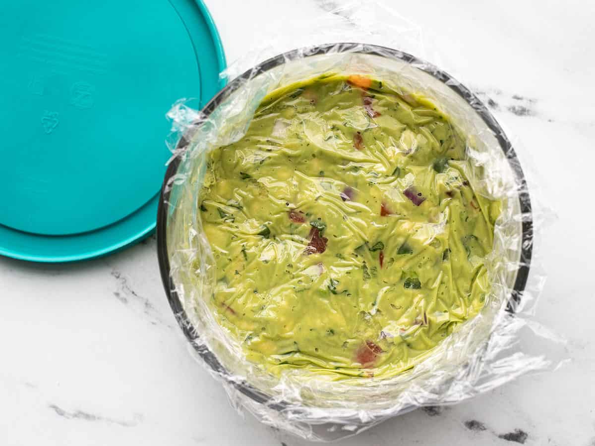 Guacamole in a bowl with plastic wrap for storage.