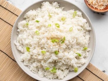 Coconut rice on a plate garnished with green onion and toasted coconut.