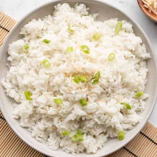 Coconut rice on a plate garnished with green onion and toasted coconut.