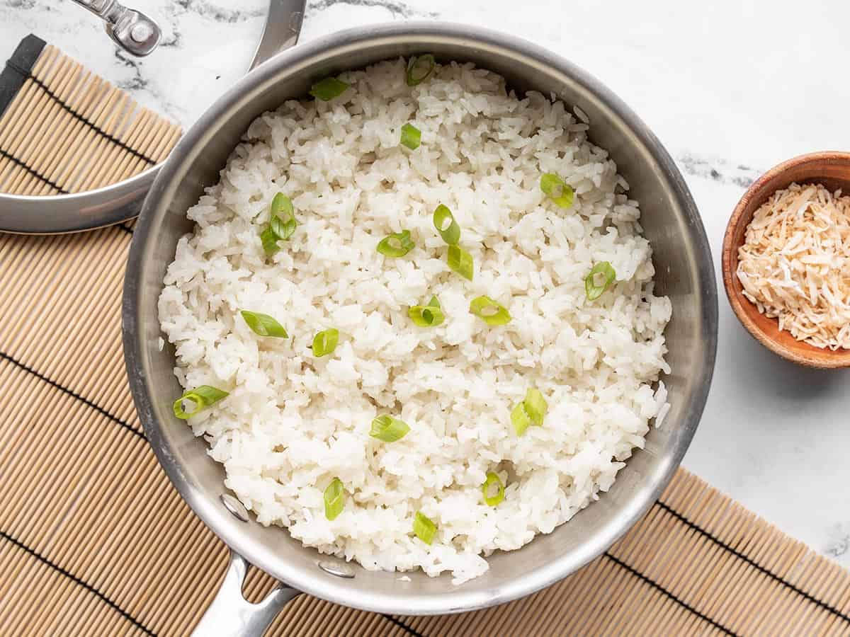 Coconut rice in a saucepot on a bamboo mat, garnish with green onion and toasted coconut.