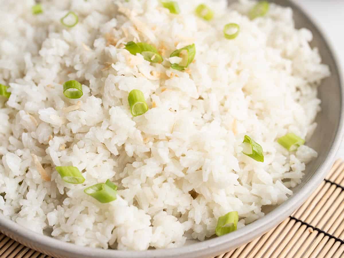 Close up side view of coconut rice on a plate, garnished with green onion and toasted coconut.