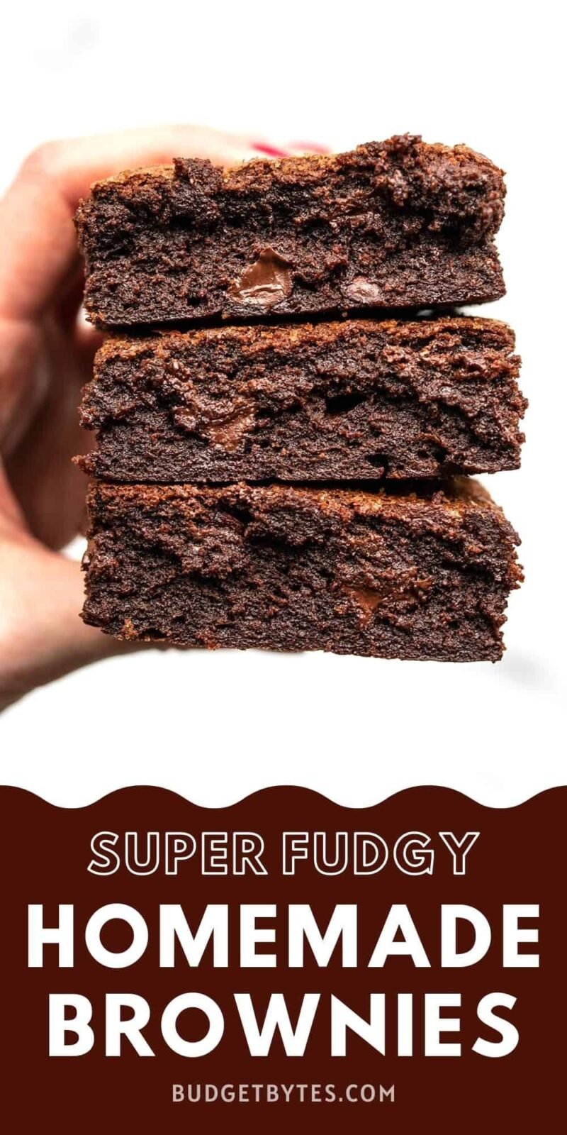 A hand holding a stack of three homemade brownies.