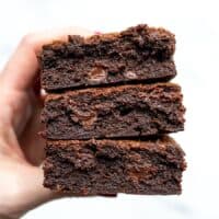 A hand holding a stack of super fudgy homemade brownies.