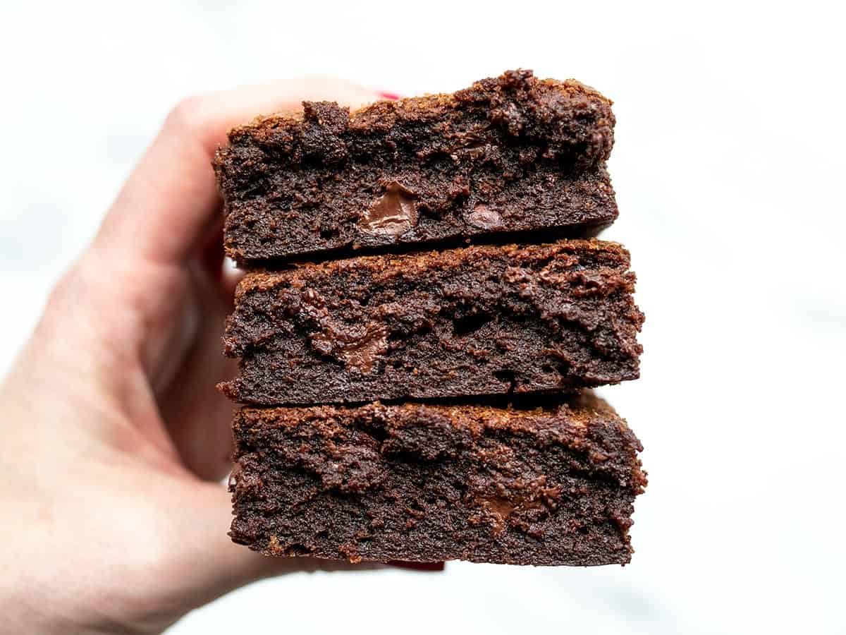 A hand holding a stack of super fudgy homemade brownies.