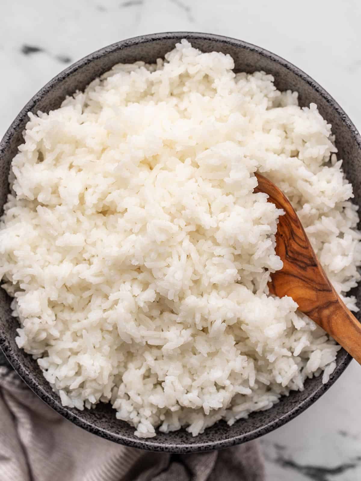 Cooked rice in a bowl with a wooden spoon.