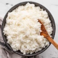 Cooked rice in a black bowl with a wooden spoon.