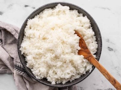 Cooked rice in a black bowl with a wooden spoon.
