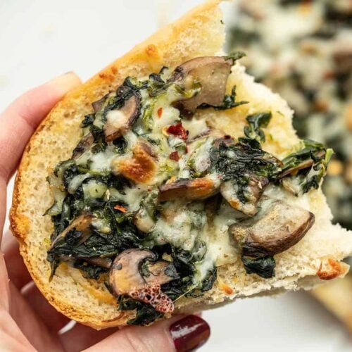 Close up of a piece of a spinach mushroom french bread pizza held in a hand.