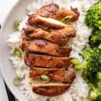 Sliced teriyaki chicken on a bed of rice next to steamed broccoli.