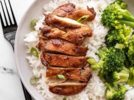 Sliced teriyaki chicken on a bed of rice next to steamed broccoli.