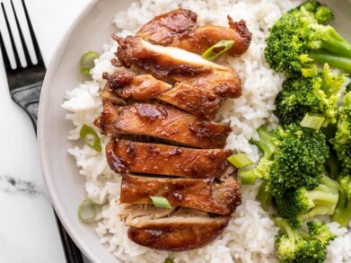 Sliced teriyaki chicken on a bed of rice next to steamed broccoli.
