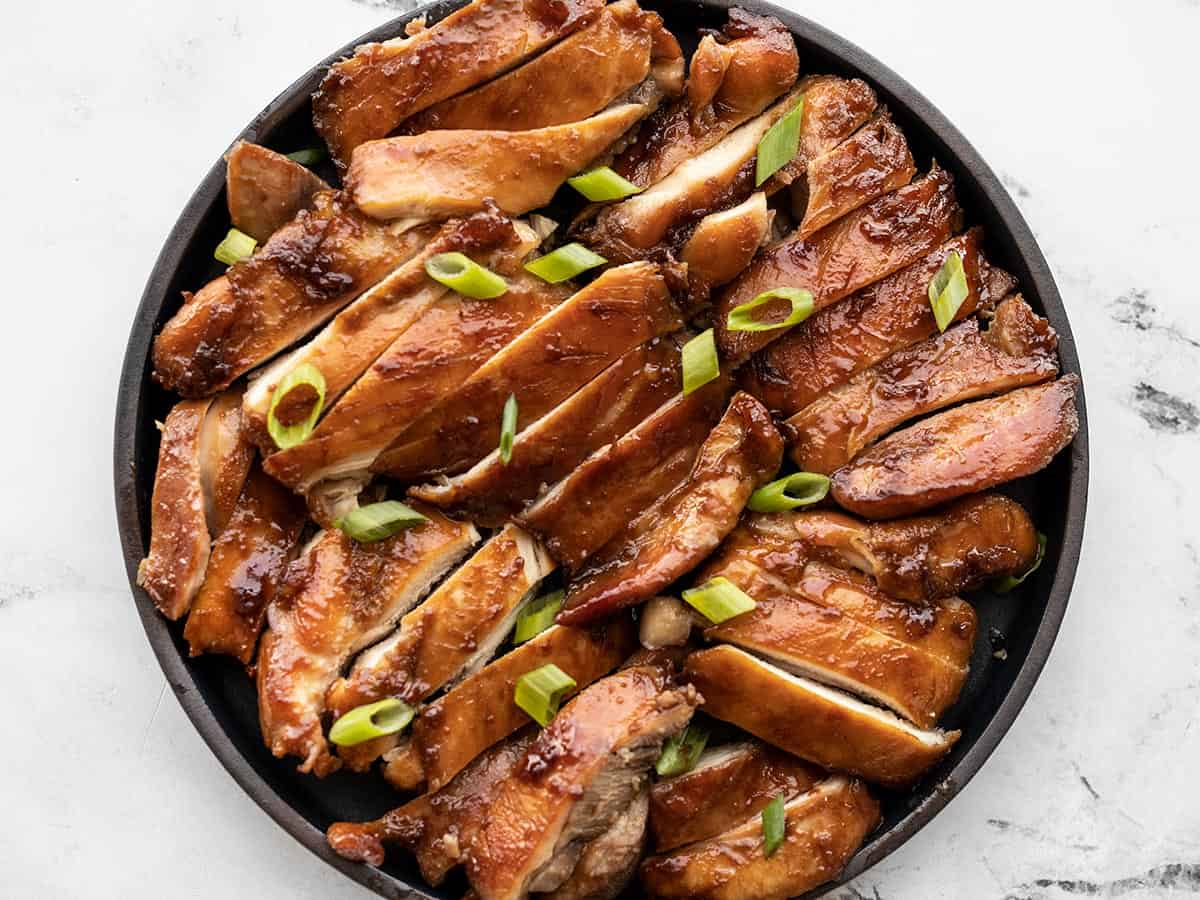 Sliced teriyaki chicken thighs on a black ceramic platter.