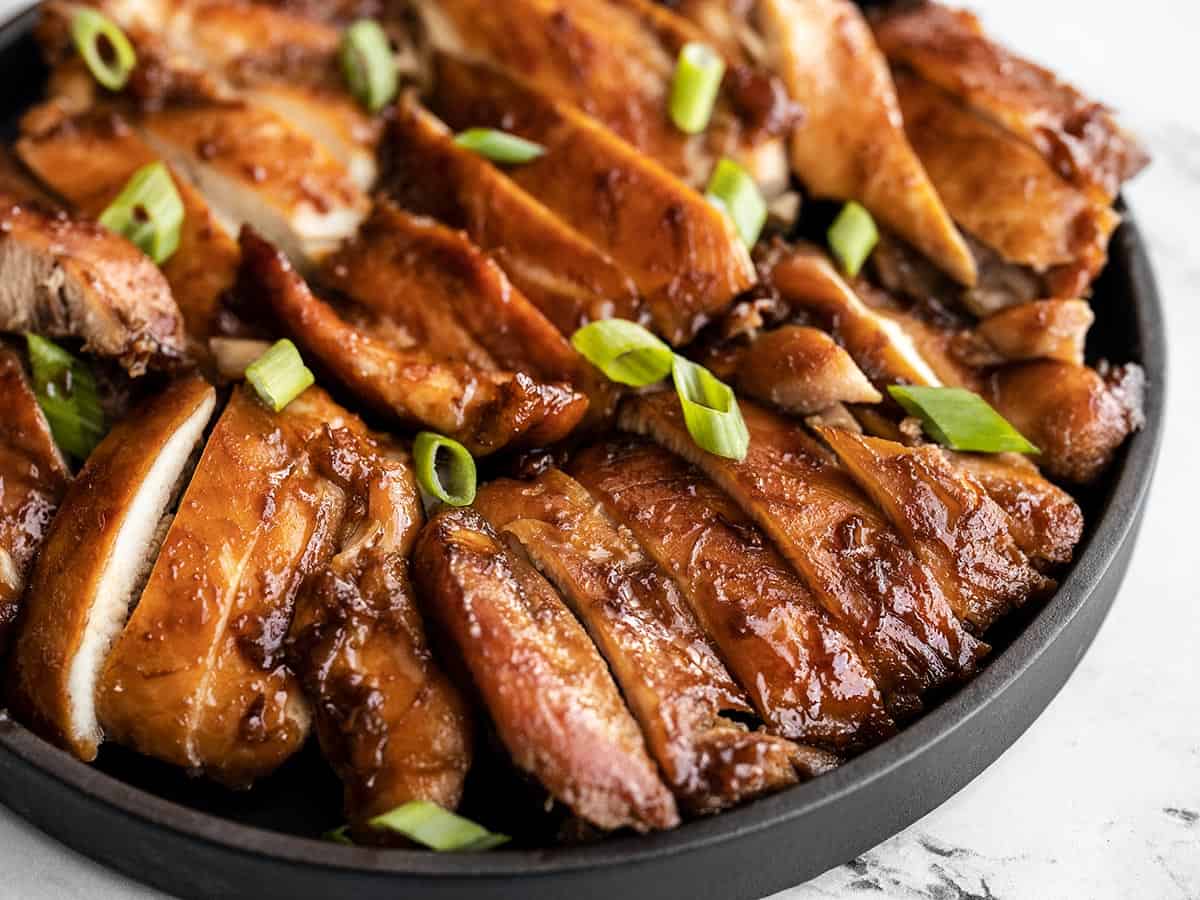 Close up side view of sliced teriyaki chicken on a platter.