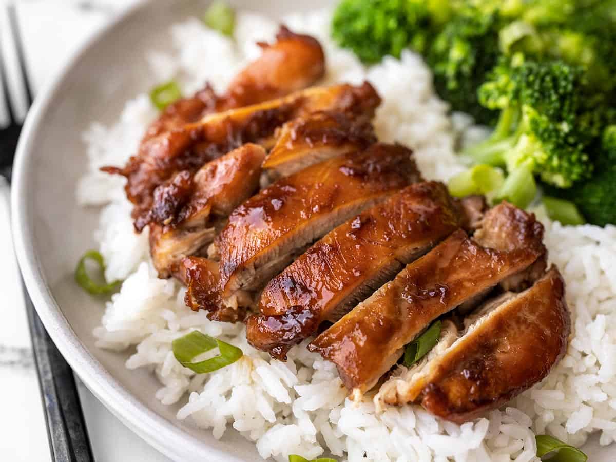 Side view of sliced ​​teriyaki chicken on a bed with rice, next to which is broccoli.