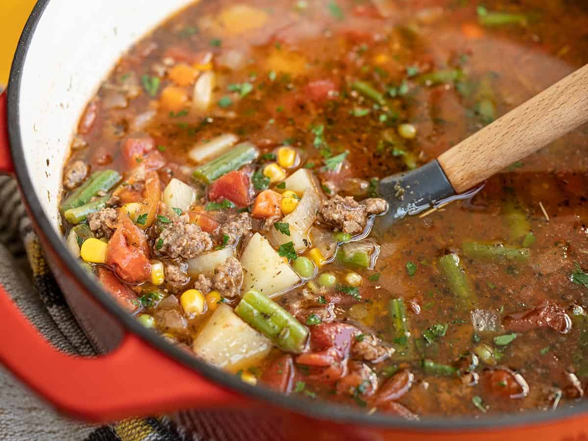 Side view of a pot of Vegetable Beef Soup with a spoon.