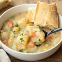 Side view of a bowl of vegetables with gravy with a piece of bread and a spoon.