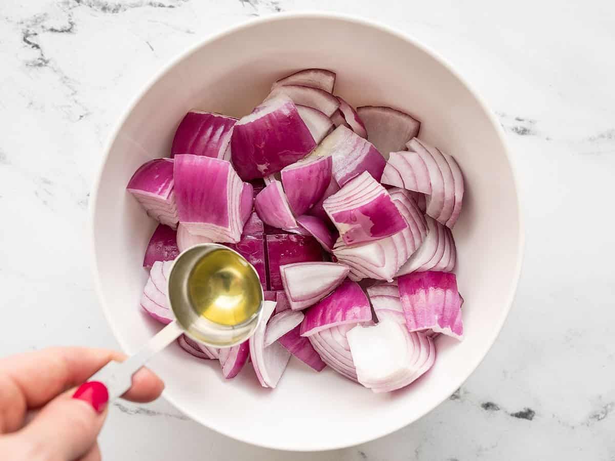 Oil being drizzled over diced red onion in a bowl.