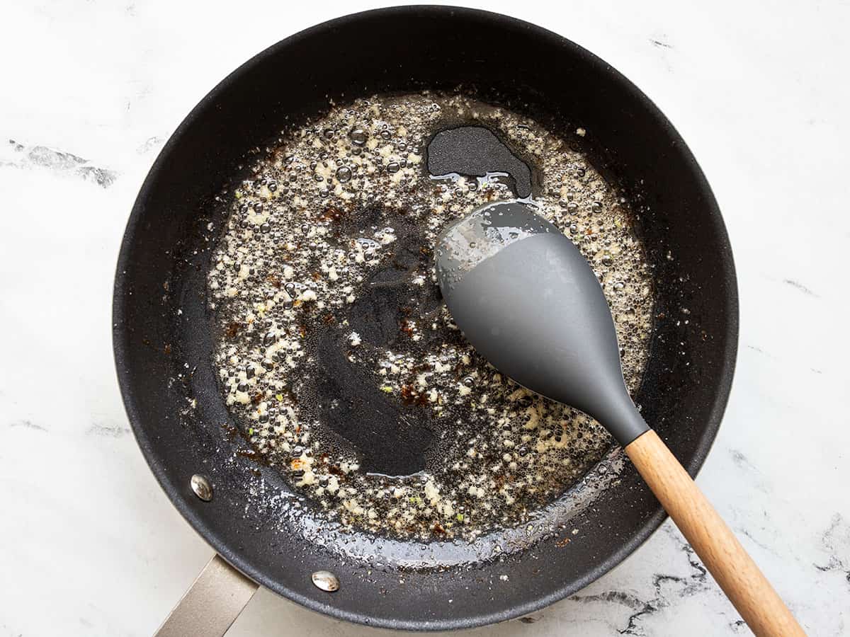 Garlic being sautéed in bacon fat in the skillet.