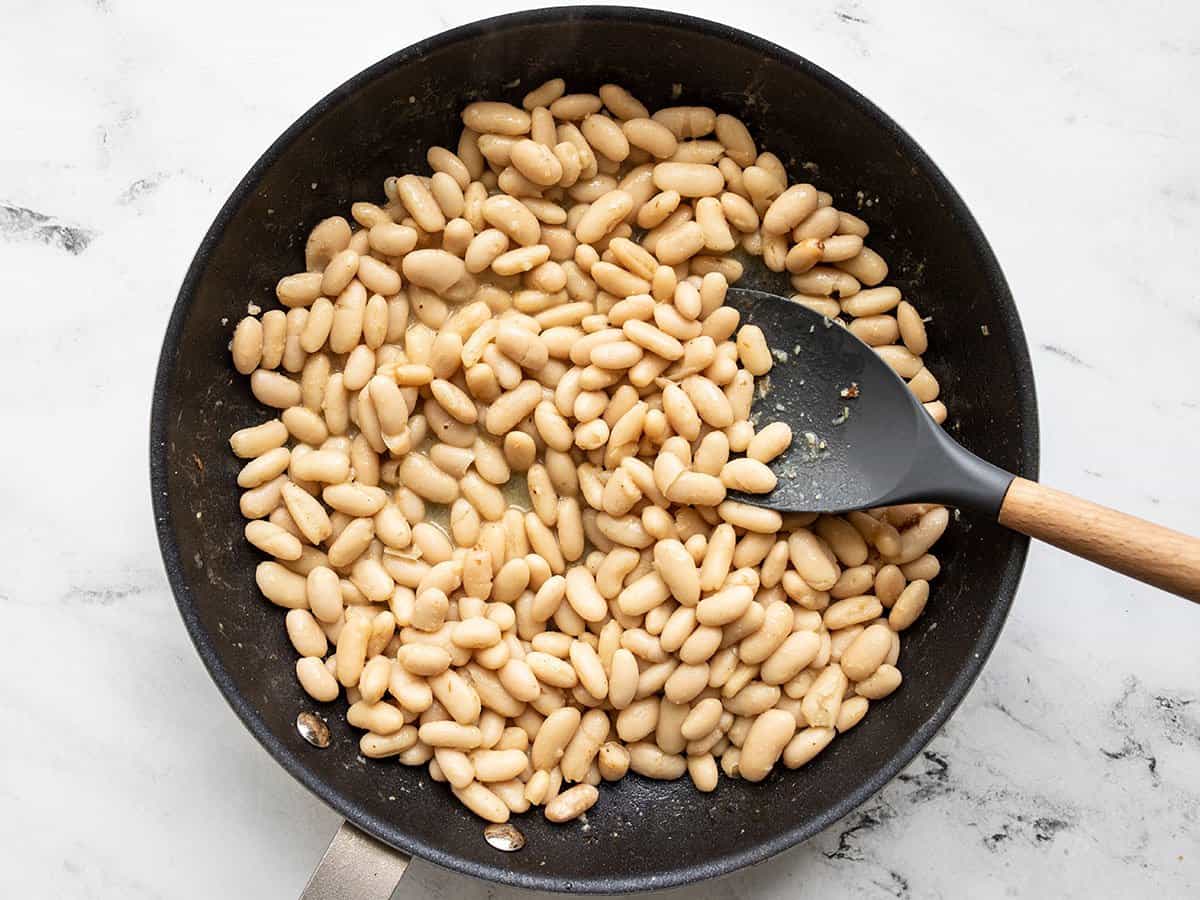 Heated beans and vinaigrette in the skillet with a spoon.