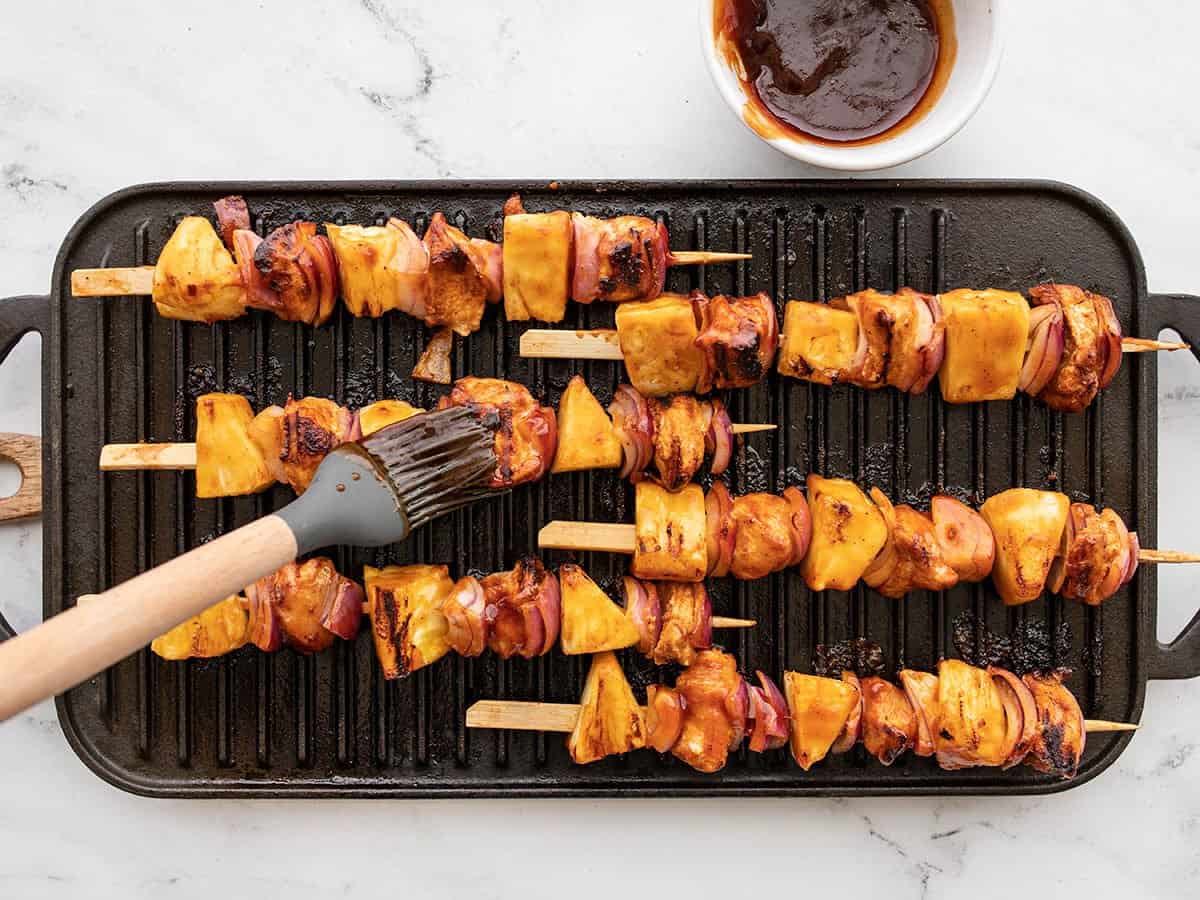 Kebabs on a grill pan being brushed with BBQ sauce.