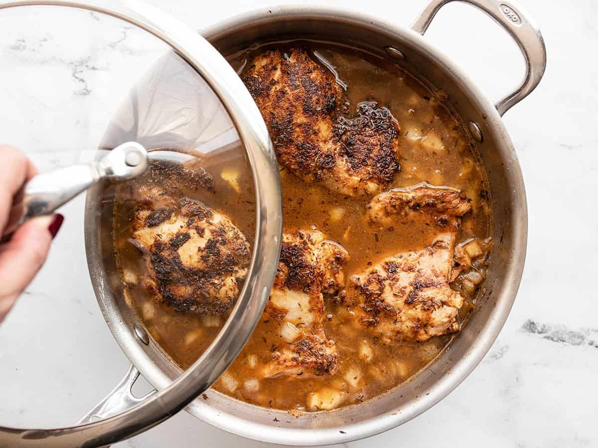 Chicken thighs back in the skillet, the lid being placed on top.