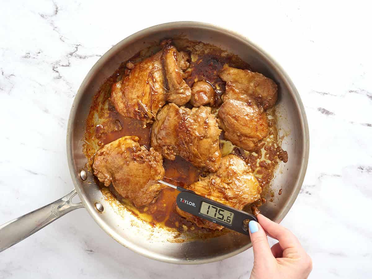 A meat thermometer being inserted into a chicken thigh to check the temperature in the skillet.