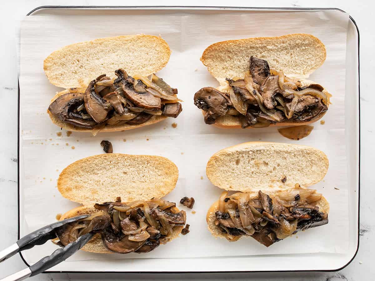 Mushrooms and onions being placed on toasted rolls.