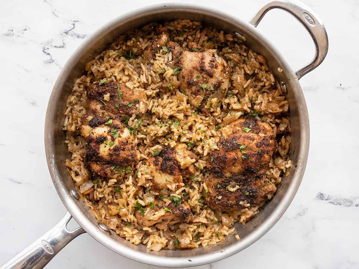 fluffed rice in the skillet with chicken thighs, garnished with parsley.